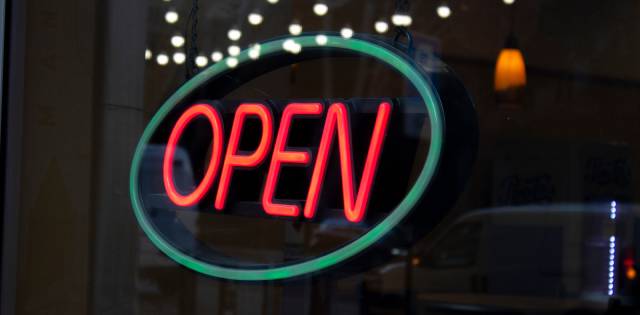 A business's glass window with a large neon sign hanging in it. A blue oval circles the bright red letters that say, "Open."