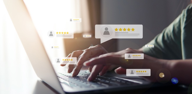A person sitting at their table typing on their laptop. There are several customer review graphics hovering the laptop.
