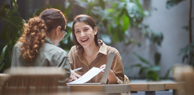 Two happy employees enjoying the outdoor terrace at their workplace. They're talking, laughing, and working.