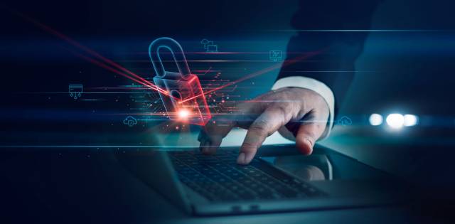 A hand of a businessman wearing a suit reaches down toward a laptop keyboard overlaid with a digital security lock.