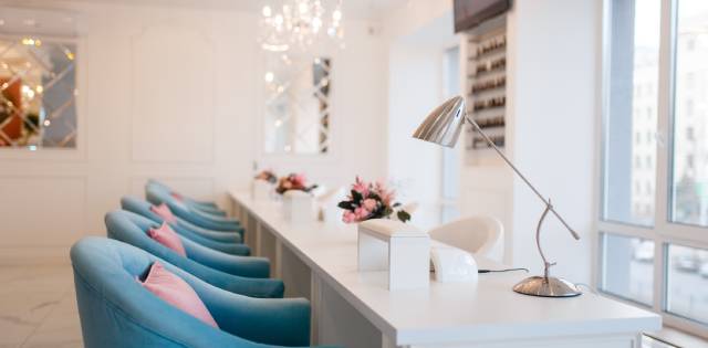 A line of blue chairs with pink pillows sitting in front of six white manicure stations at a beauty salon.
