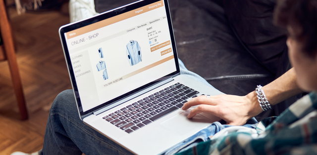 A person with a laptop in their lap browsing on an online clothing store’s website and looking at a blue dress shirt.