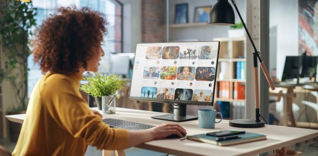 A startup manager sitting at her desk using the computer to review social media content and plans. She's smiling.