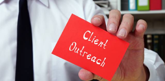 A business professional in a button-up shirt and tie holding up a small red business card that reads “Client Outreach.”
