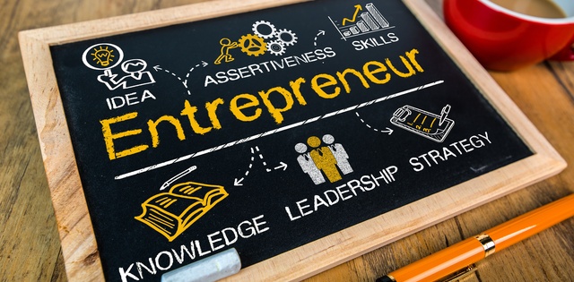 A small chalkboard on a wooden table features the word 'Entrepreneur' in yellow, surrounded by related business terms.
